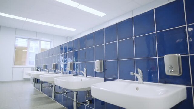 Spacious washroom displays orderly line of washbasins with glossy tiles. Sterile design creates functional environment for hand hygiene
