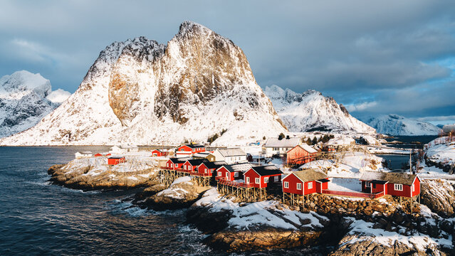 Red rorbuer cabins below dramatic winter peaks in Hamnoy, Lofoten Islands, Norway
