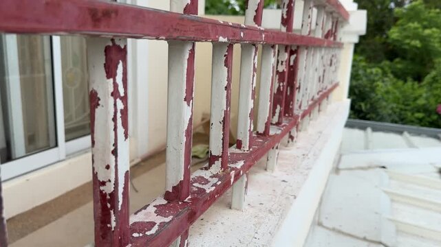 Weathered metal balcony railing with peeling paint and rust showing aging deterioration and maintenance issues.