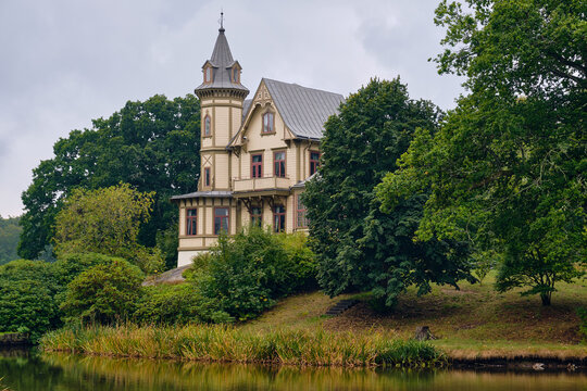 Ronneby, Sweden - 11 September 2025: View of Brunssparken featuring a historic 19th-century wooden villa nestled among lush trees and reflecting in the calm park pond.