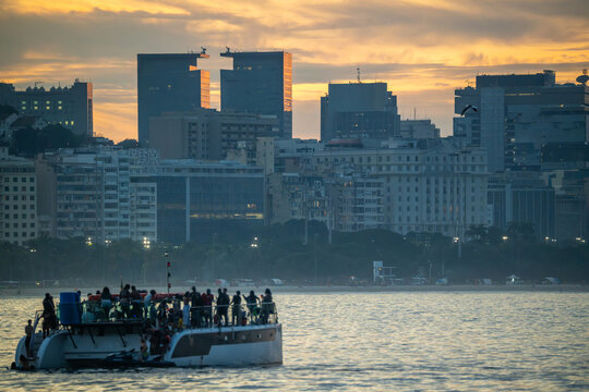 Rio de Janeiro, Rio de Janeiro, Brazil - 20 June 2026: View of a crowded catamaran sailing on the water with the Rio de Janeiro city skyline in the background during a golden sunset.
