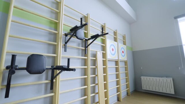 Wall bars with dip stations and targets mounted in gym. Sports facility offers various equipment for training along with strength exercises