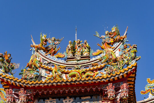 Taipei, Taiwan - 15 January 2026: View of an ornate temple roof featuring colorful ceramic dragons, mythical figures, and intricate carvings against a clear blue sky.
