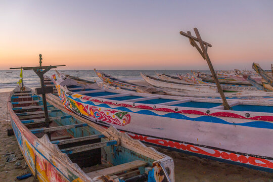 Fishing boats on sandy shore of Port de Peche in Nouakchott, Mauritania at sunset highlight traditional maritime life in West African capital.
