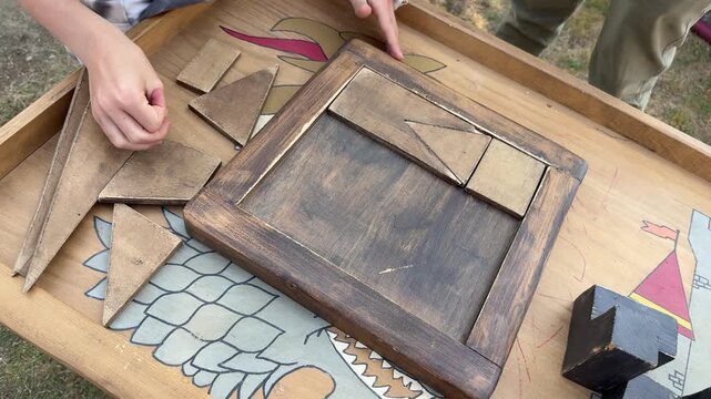 Hands solving wooden geometric puzzle, tabletop brain teaser close up