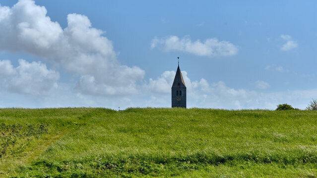 Den Oever, Netherlands - 20 May 2026: View of the Churchtower of Oosterland rising above a green sea dike under a blue sky with white clouds on the former island of Wieringen.