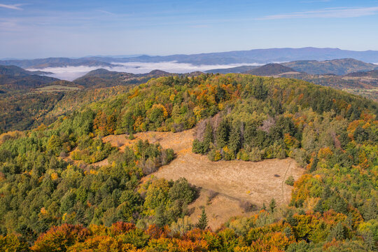 Aerial view of Sitno mountain landscape in autumn, with colorful forests, dry grassland, and distant rolling hills under a clear blue sky in Ilija, Banska Bystrica Region, Slovakia.