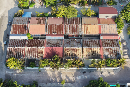 Aerial view of a row of houses with weathered, rusty corrugated metal roofs, surrounded by lush palm trees and tropical vegetation in Kudahuvadhoo, Dhaalu Atoll, Maldives.