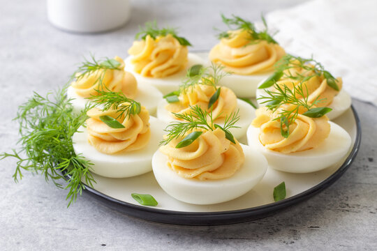 Boiled eggs stuffed with garlic and mayonnaise filling, garnished with fresh dill and green onion. Protein rich appetizer served on a plate, close up view