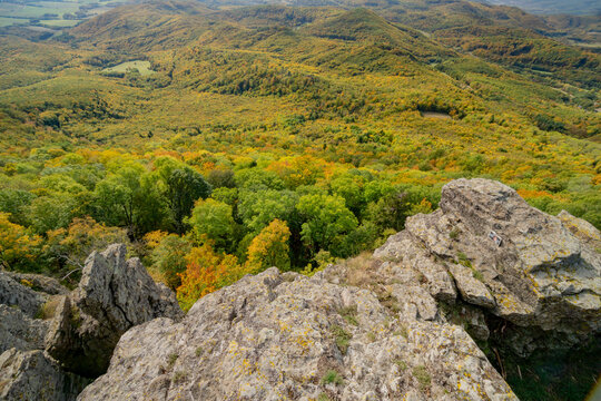 Aerial view of Sitno in Stiavnicke Vrchy featuring rocky cliffs overlooking a vast expanse of dense autumn forest with vibrant foliage in Ilija, Banska Bystrica Regio, Slovakia.