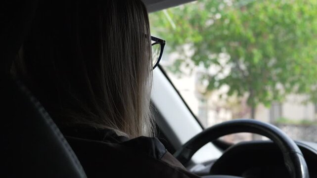 Driver car woman driving through urban streets on a bright day viewed from the back seat of the vehicle