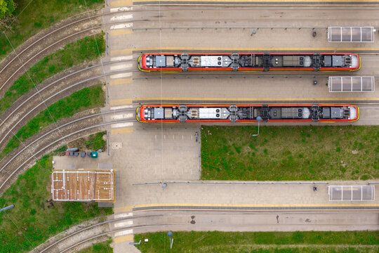 Aerial view of modern trams parked at a depot with parallel tracks, paved platforms, and surrounding green spaces in Warsaw, Mazowieckie, Poland.