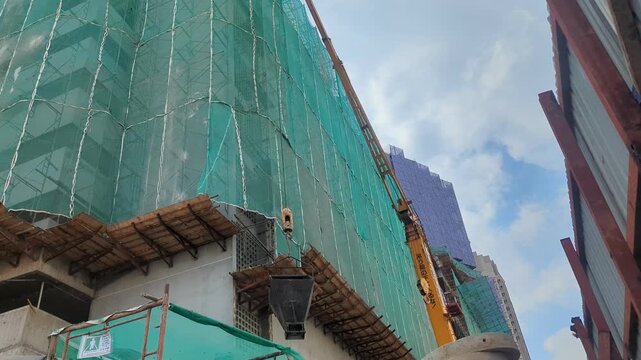 Low-angle shot of a construction crane working on a high-rise building under development, covered in green safety netting.