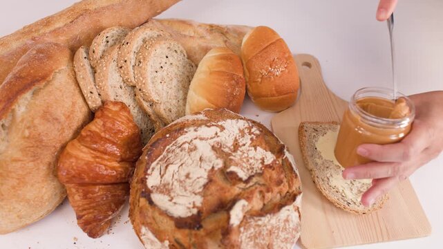 Spreading Creamy Peanut Butter on Sliced Multigrain Bread with Assorted Pastries