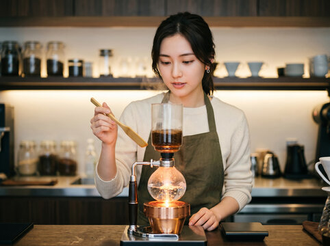 モダンなカフェの厨房でサイフォン抽出を見つめる女性