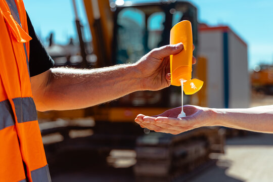 Bauarbeiter spritzt Sonnencreme auf eine Hand