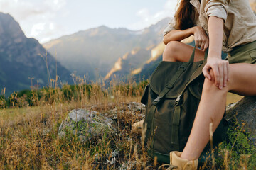 Obraz premium Young woman traveler with backpack resting on rock in mountain field holding hand of companion during outdoor adventure in sunny nature landscape.