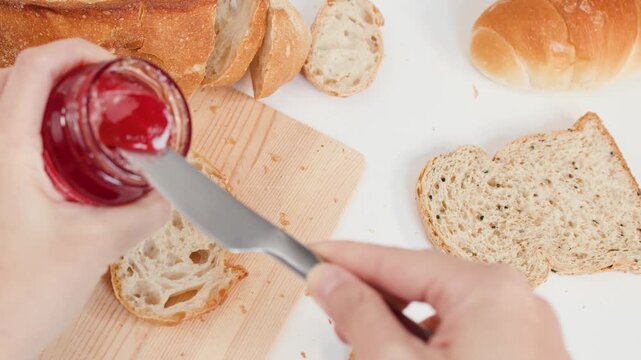Spreading Red Strawberry Jam on Sourdough Bread Slice with Knife
