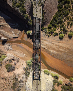 Aerial view of a historic railway bridge spanning a dry riverbed in an arid desert landscape with sparse vegetation and rocky terrain in Argentina.