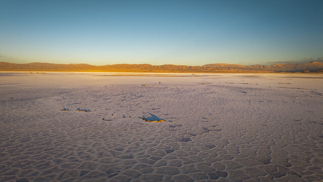 Aerial view of Salinas Grandes salt flats with a vast cracked surface under a clear blue sky at sunset in La Poma Department, Salta Province, Argentina.