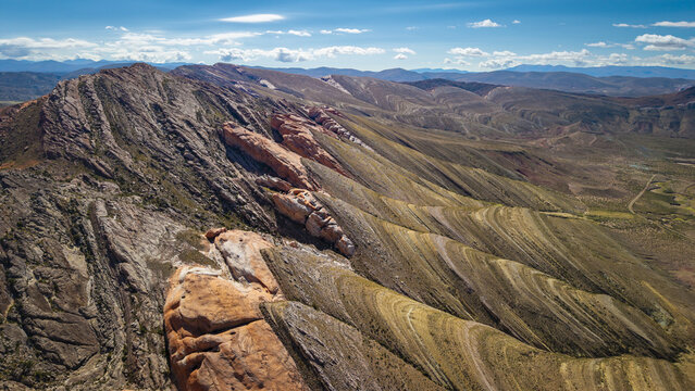 Aerial view of Gigantes Dormidos geological formations with dramatic layered sedimentary rock and arid mountain ridges under a blue sky in Tres Cruces, Jujuy Province, Argentina.