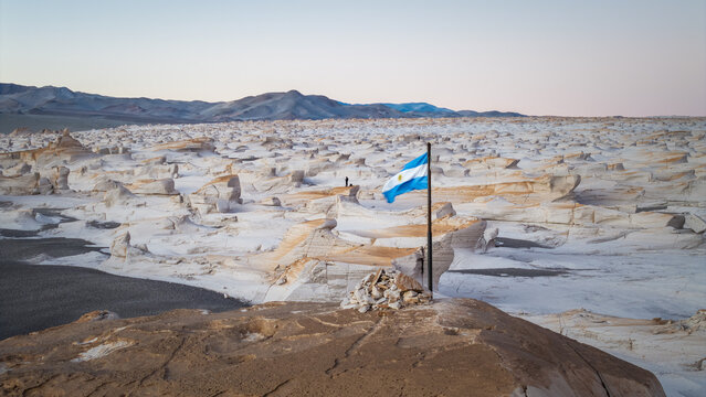 Aerial view of the vast white pumice stone formations with an Argentine flag waving in the foreground in El Penon, Catamarca Province, Argentina.