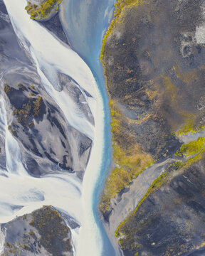 Aerial view of a glacial braided river with intricate sediment patterns, dark volcanic sand banks, and vibrant green mossy patches in Selfoss, Sveitarfelagid Arborg, Iceland.