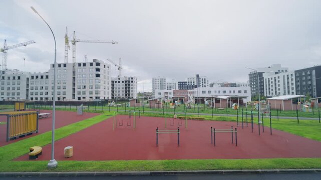 Large glass frame overlooks urban courtyard with various exercise equipment. New apartment buildings create fresh architectural landscape