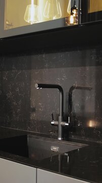 Vertical video. Black kitchen with wood cabinetry, gas stove, sink and dark countertop design.