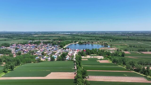 Aerial view of rural settlement with lake farmland and green fields under clear blue sky