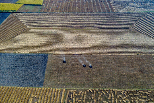 Aerial view of agricultural fields with harvested crops and small fires burning in Panchagarh, Rangpur Division, Bangladesh.