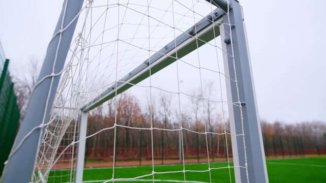 Football goal structure stands on professional synthetic pitch closeup. Overcast weather and urban buildings create modern sports scene