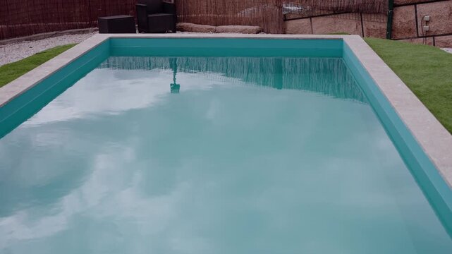 Clean turquoise rectangular swimming pool with waterfall edge filling in private backyard garden