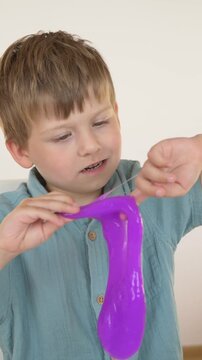 Boy stretches stringy purple slime between his fingers, exercising fine motor skills and hand coordination during calm sensory play session that helps develop grip strength and focus. 