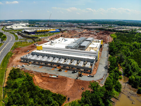 Aerial view of a large data center construction site with heavy machinery, exposed earth, and surrounding forest in Ashburn, Virginia, United States.