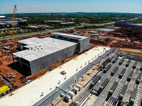 Aerial view of a large data center construction site featuring concrete buildings, industrial cooling units, construction cranes, and earthworks in Ashburn, Virginia, United States.