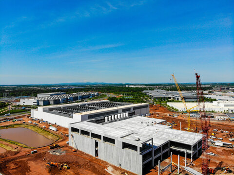 Aerial view of a large data center construction site featuring concrete structures, tall cranes, and heavy machinery, set against a clear blue sky in Ashburn, Virginia, United States.