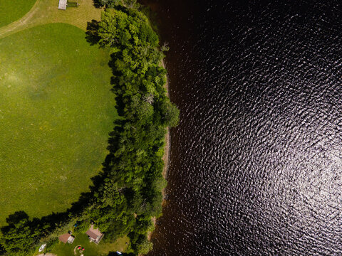 Aerial view of the shoreline of Commanda Lake with lush green trees bordering a grassy lawn and dark rippling water in Restoule, Ontario, Canada.