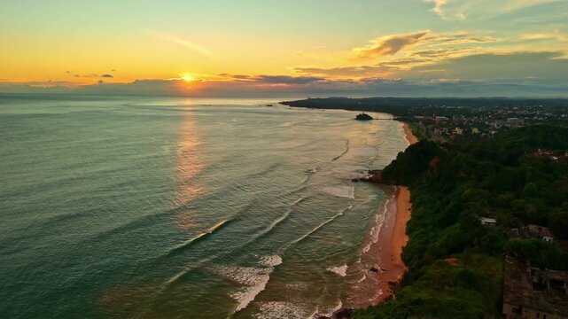 Sunset light reflects across the Indian Ocean as gentle surf meets the long shoreline and green headland at Madiha Beach.