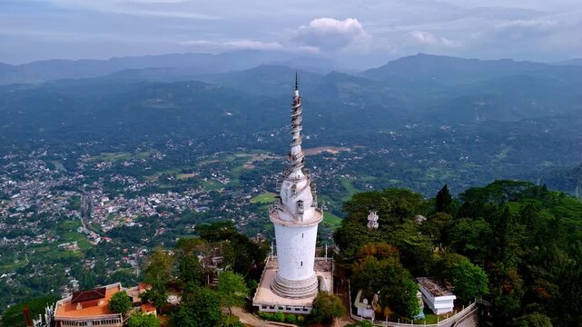 Tall pagoda-like structure crowns a wooded ridge as the camera flies past, revealing a broad Sri Lankan highlands valley below.