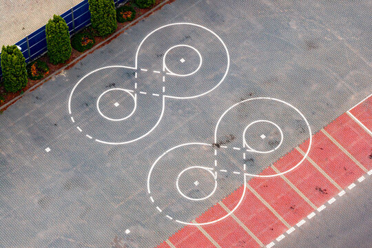 Aerial view of two white infinity-shaped markings painted on a paved parking lot with green bushes and a blue fence in Warsaw, Masovian Voivodeship, Poland.