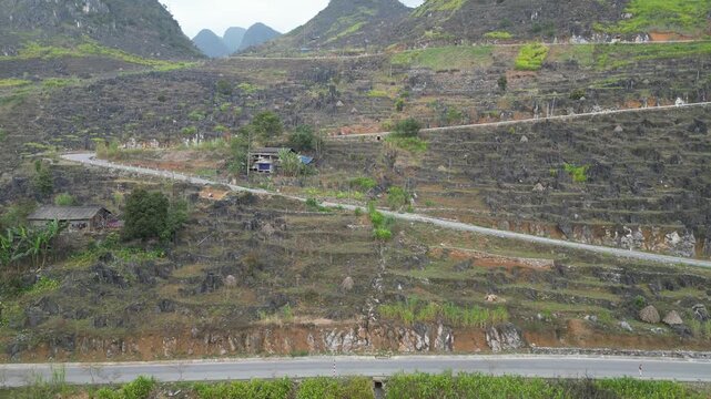 Aerial drone view of terraced limestone hillsides, rural homes and mountain roads crossing the rugged terrain of the Dong Van Karst Plateau in Ha Giang Vietnam