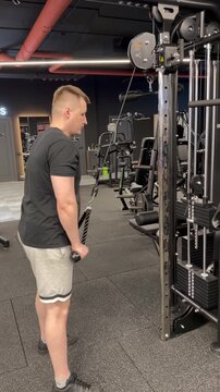 Athletic man performing a rope triceps pushdown on a cable machine in a modern gym, building upper-body strength and arm muscles