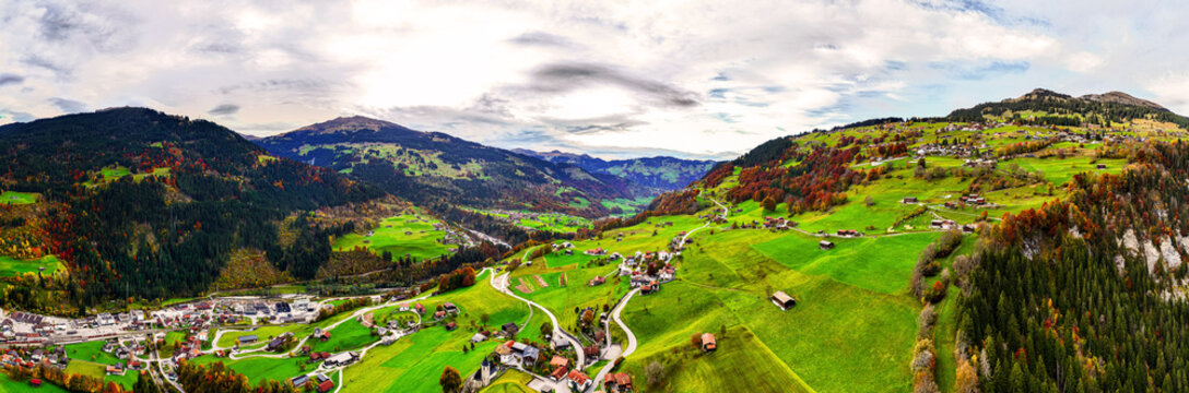 Aerial view of the village of Klosters-Serneus with traditional chalets, winding roads, and autumn foliage on the surrounding slopes in Klosters-Serneus, Grisons, Switzerland.