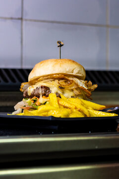 Gourmet beef burger with golden fries on a black plate, fresh fast food meal