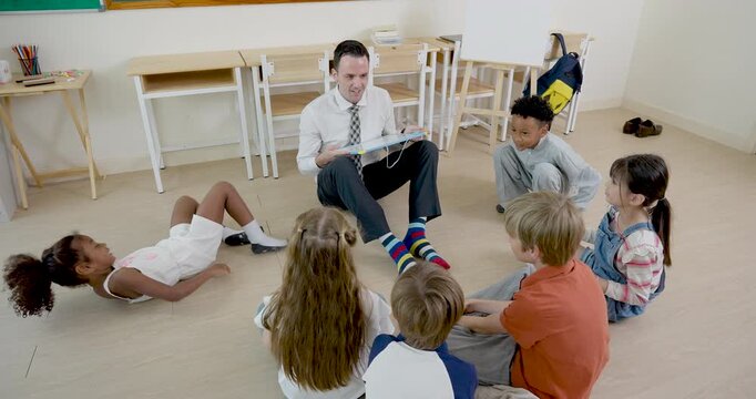 Young boy student stands from floor circle to answer male adult teacher during back to school primary lesson, while multicultural pupil group listens and builds confidence, readiness and respect