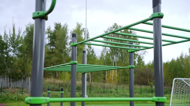 Monkey bars and metal workout frames at sports park. Equipment features professional grey and green finish set against soccer goal