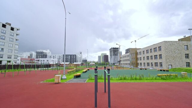 New workout area sits next to modern school under overcast sky. Urban development projects create busy skyline for developing community zone