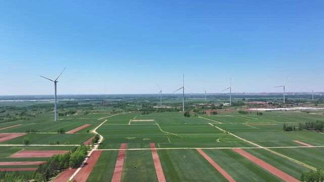 Multiple wind turbines stand tall in green farmland under a clear blue sky