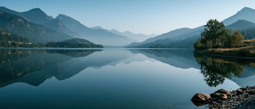 Escape into stillness glassy alpine lake mirrors mist layered mountains under a clear blue sky. Ideal for wellness, mindfulness, travel, and eco conscious campaigns seeking pure natural.